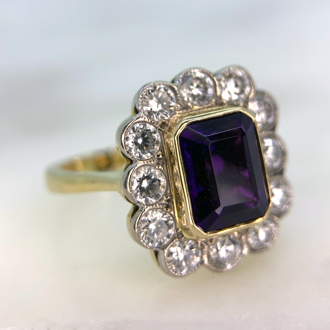 Vintage Amethyst and Diamond Rectangular Cluster Ring in 750 (18ct) Yellow Gold, hallmarked Birmingham. The rectangular cut Amethyst measures approximately 9.5mm x 7.25mm with a colour variation from deep to pink purple. Surrounding the amethyst is 12 brilliant cut Diamonds.  All stones are in rub over settings. As you look on the top of the ring it  measures 18.5mm X 16.25mm. Ring in immaculate condition. 
