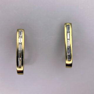 Baguette Diamond Earring Studs in 18ct Gold. The baguette diamonds are channel set, in gold that loops under the lobe. The earrings measure 15.5mm x 2.3mm and are in excellent condition.  Age: Modern Material: Gold Carat: 18ct, Yellow Weight: 3.2g Dimensions: Width 2.3mm, Length 15.5mm