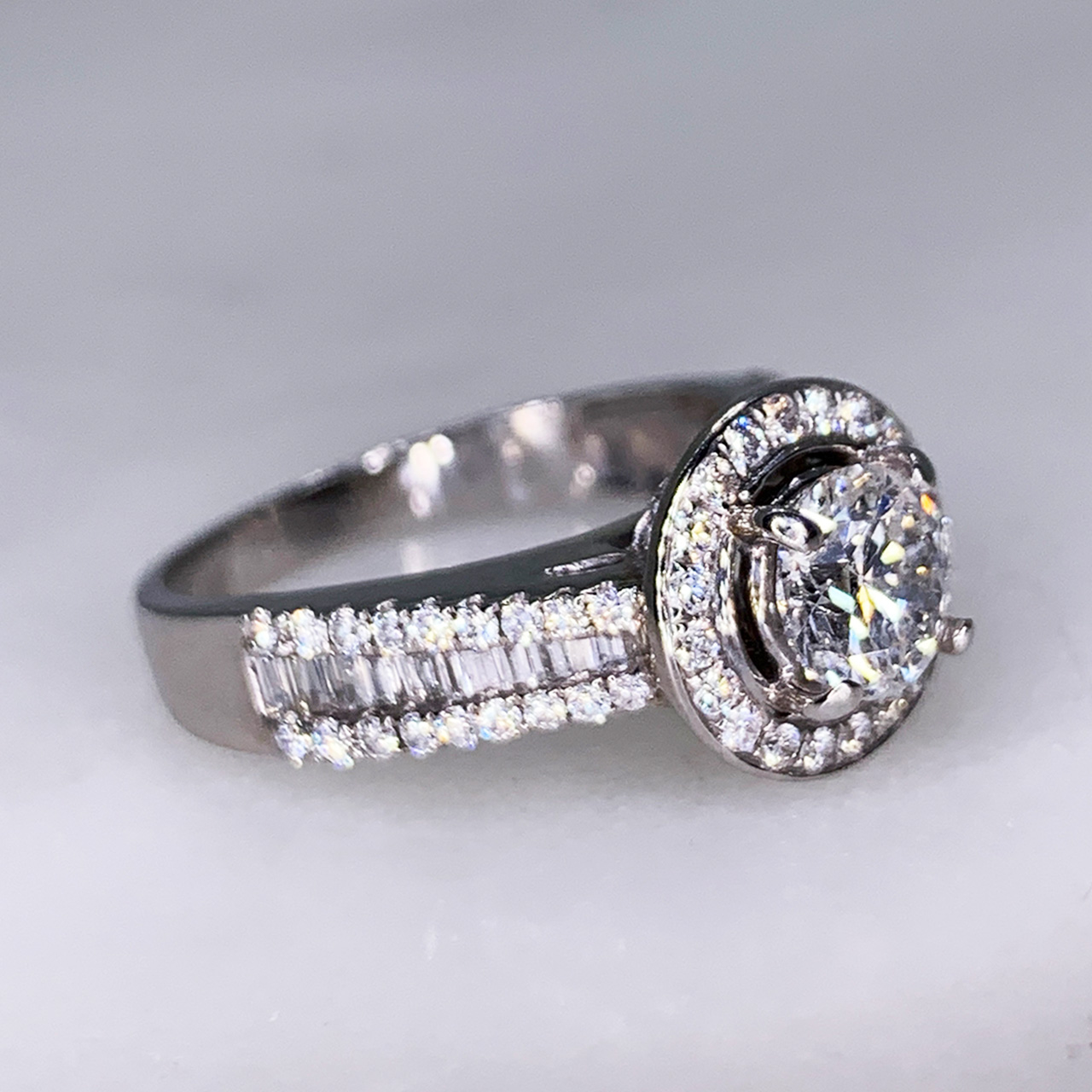 Stunning Diamond Halo Cluster Ring in 18ct White Gold, Stamped 750 (for 18ct) in the shank. The central Diamond 0.77cts is claw set and surrounded by a cluster of diamonds. This ring is beautifully detailed with geometric baguette and round diamond set shoulders and diamond set detail underneath the top of the central setting. 