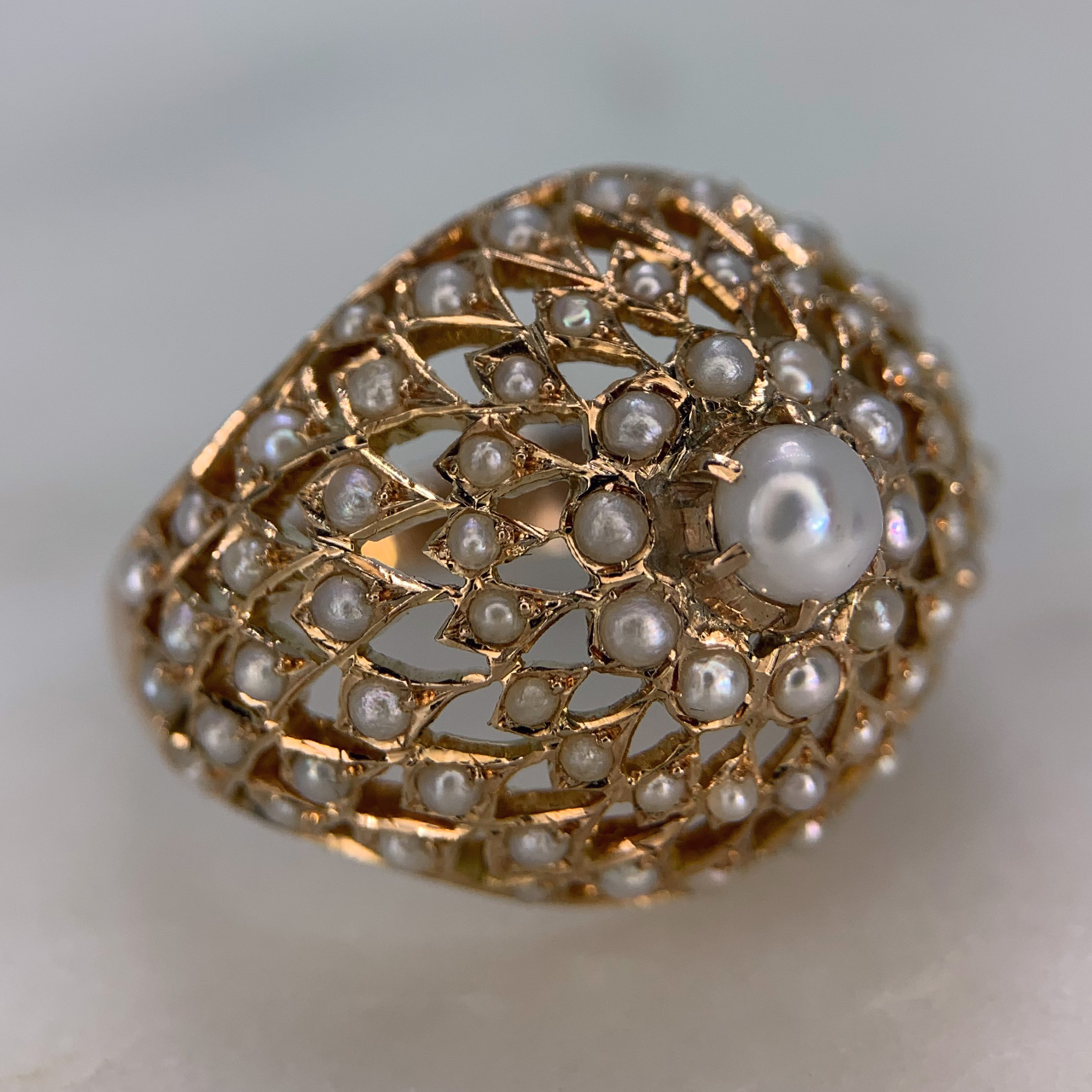 Unusual Pearl Bombe Ring in stamped 9ct Rose Gold. The ring head is domed and pierced in shape, and set with half pearls. The ring has one central pearl at 4.45mm in diameter and is surrounded by 6 bands of half pearls equating to 81 set pearls. Exquisite condition. 